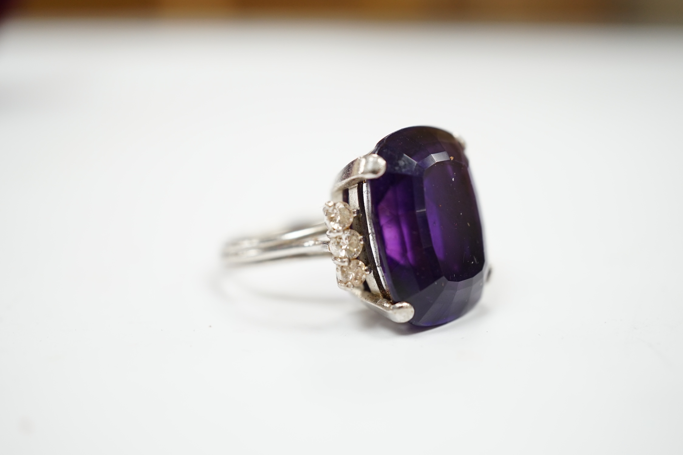 A white metal and single stone cushion cut amethyst set dress ring, with six stone diamond set shoulders, size O, gross weight 9.2 grams.